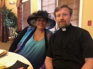 woman in hat and gloves with Fr. Kurtis Wiedenfeld at Centennial Tea